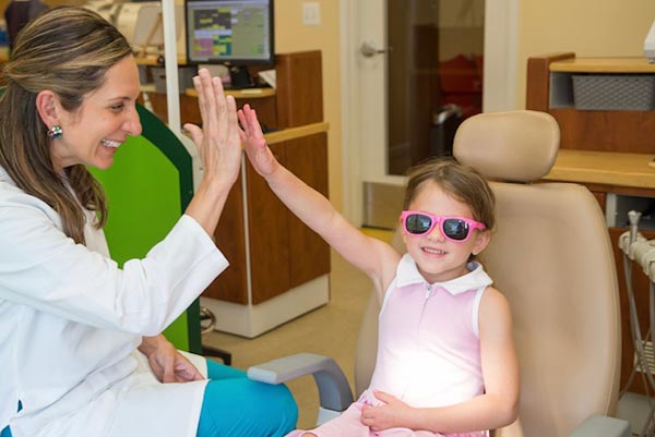 Dentist and patient high-fiving each other. Patient is a young girl in a chair, smiling as she high-fives the female dentist.