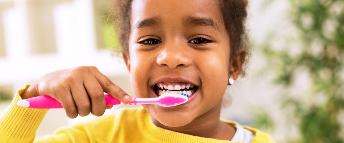 Little girl in full frame of the image, happily brushing her teeth with a bright pink toothbrush.