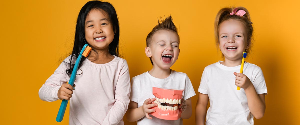 Three children, two girls and a boy, smiling and laughing while holding dentist equipment toys.