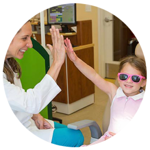 Dentist and patient high-fiving each other. Patient is a young girl in a chair, smiling as she high-fives the female dentist.